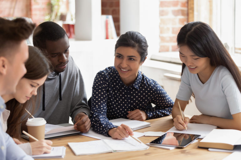 Diverse group of five students gathered around a table studying.